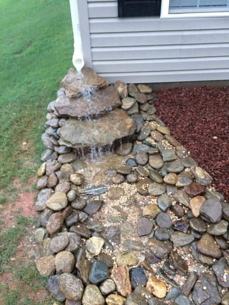 Downspout draining into a stone-lined drainage channel next to a house